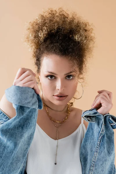 Portrait of stylish model in denim jacket looking at camera isolated on beige — Stock Photo