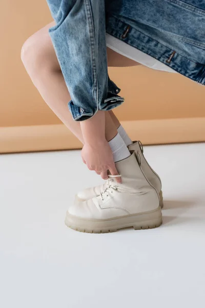 Cropped view of young woman touching stylish boots on beige background — Stock Photo