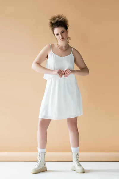 Full length of young woman in boots and white clothes on beige background — Stock Photo