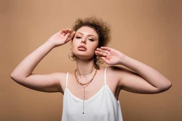 Mujer bonita en top blanco mirando a la cámara aislada en beige - foto de stock