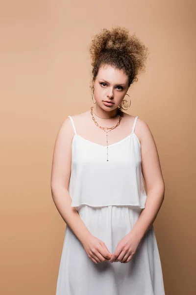 Stylish model in white clothes and necklaces looking at camera isolated on beige — Stock Photo