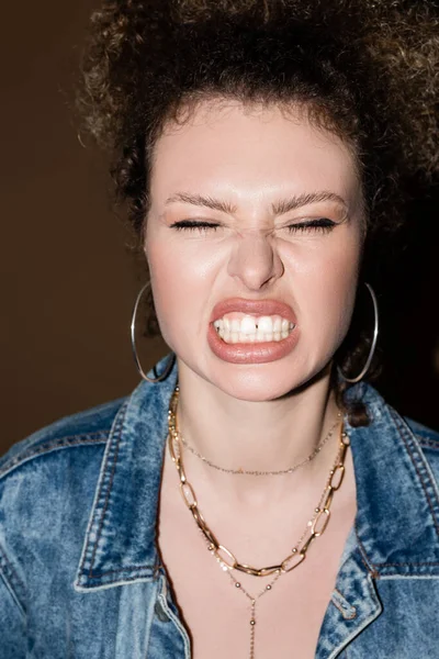 Modelo enojado en chaqueta vaquera y accesorios que muestran los dientes sobre fondo negro - foto de stock