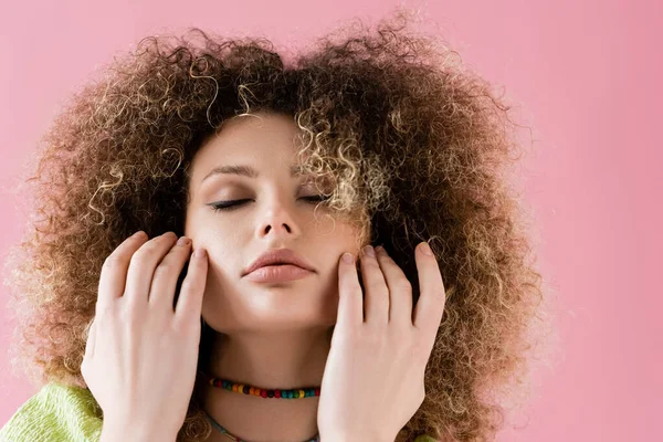 Modèle bouclé avec les yeux fermés touchant le visage isolé sur rose — Photo de stock