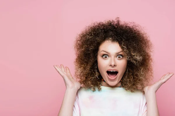 Schockierte lockige Frau blickt isoliert auf rosa Kamera — Stockfoto