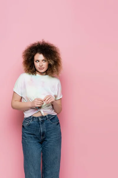 Giovane modello riccio in jeans e t-shirt distogliendo lo sguardo su sfondo rosa — Foto stock