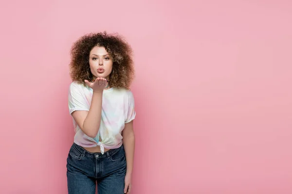 Curly woman blowing air kiss at camera isolated on pink — Stock Photo
