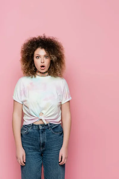 Femme choquée en t-shirt et jeans regardant la caméra isolée sur rose — Photo de stock