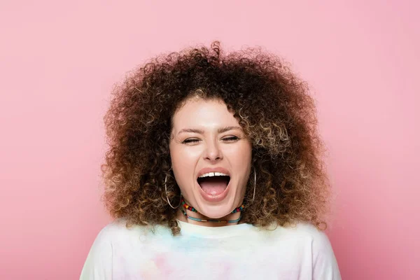 Excited curly woman in t-shirt closing eyes isolated on pink — Stock Photo