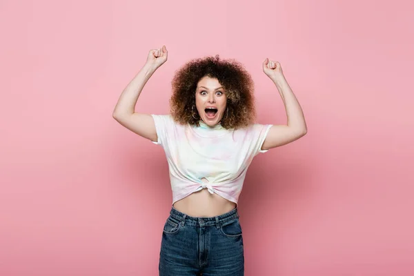 Возбужденная женщина в джинсах и футболке показывает да жест показывая на розовом фоне — стоковое фото