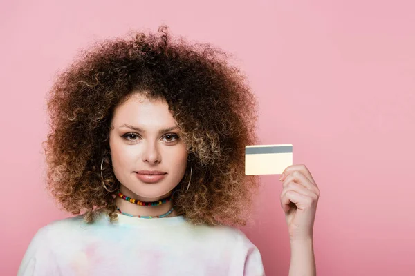 Donna riccia in possesso di carta di credito e guardando la fotocamera isolata su rosa — Foto stock