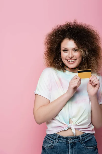 Mulher alegre em t-shirt segurando cartão de crédito em fundo rosa — Fotografia de Stock