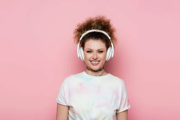 Mulher sorridente em camiseta e fones de ouvido isolados em rosa — Fotografia de Stock