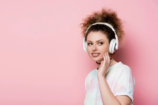 Усміхнена жінка в навушниках дивиться ізольовано на рожевий — стокове фото