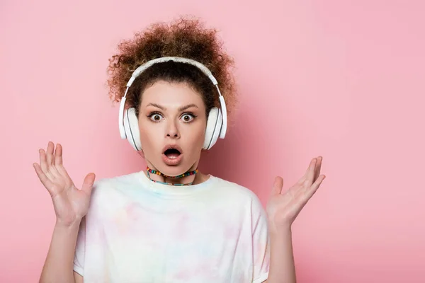 Mujer sorprendida en los auriculares mirando a la cámara en el fondo rosa - foto de stock