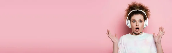 Shocked woman in headphones looking at camera on pink background, banner — Stock Photo