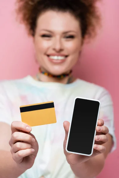 Mujer borrosa sosteniendo teléfono inteligente y tarjeta de crédito aislada en rosa - foto de stock