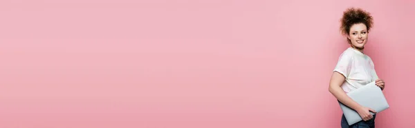 Alegre freelancer sosteniendo portátil aislado en rosa, bandera - foto de stock