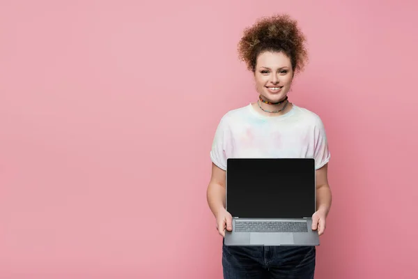 Femme gaie tenant ordinateur portable avec écran blanc isolé sur rose — Photo de stock