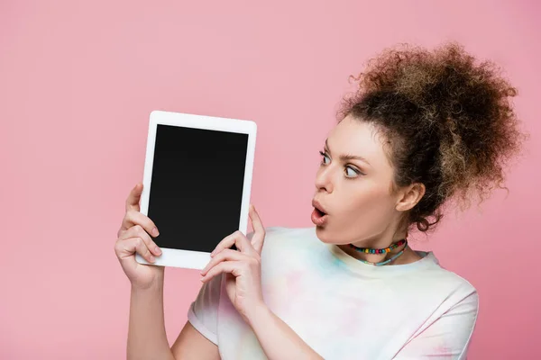 Mujer conmocionada mirando tableta digital con pantalla en blanco aislada en rosa - foto de stock