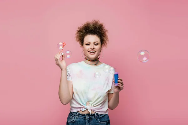 Smiling woman holding soap bubbles on pink background — Stock Photo
