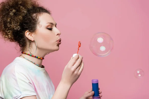 Молодая женщина надувает мыльные пузыри на розовом фоне — стоковое фото
