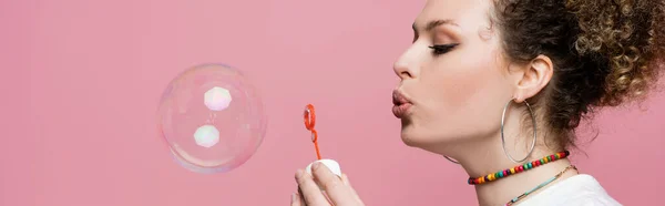 Curly woman blowing soap bubble on pink background, banner — Stock Photo