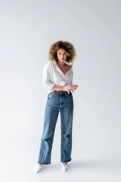 Pleine longueur de femme en jeans et chemisier regardant la caméra sur fond blanc — Photo de stock