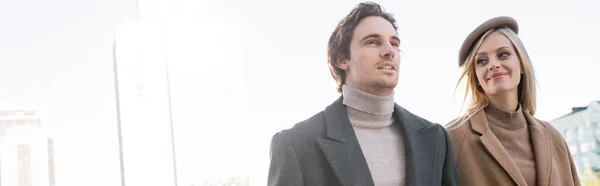 Pareja joven positiva en ropa de otoño sonriendo en la ciudad, pancarta - foto de stock