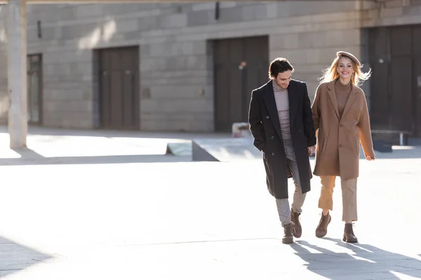 Comprimento total de casal sorridente na roupa de outono na moda de mãos dadas e andando ao ar livre — Fotografia de Stock