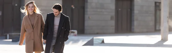 Alegre pareja en elegante otoño abrigos cogidos de la mano mientras camina en la ciudad, bandera - foto de stock