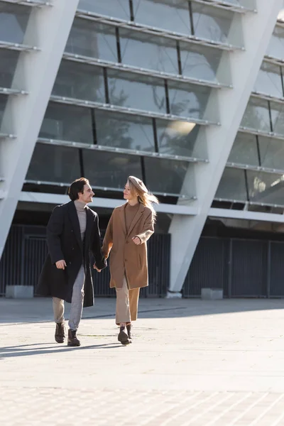 Full length of couple in coats and leather boots holding hands while walking on street — Stock Photo