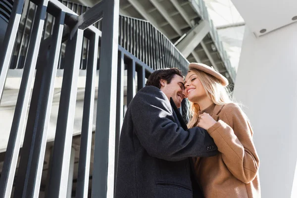 Low angle view of romantic couple with closed eyes embracing near fence in city — Stock Photo