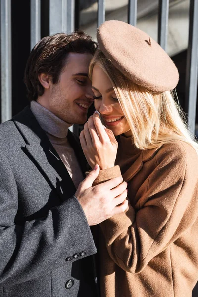 Jeune homme toucher la main de la femme souriante dans le béret à l'extérieur — Photo de stock