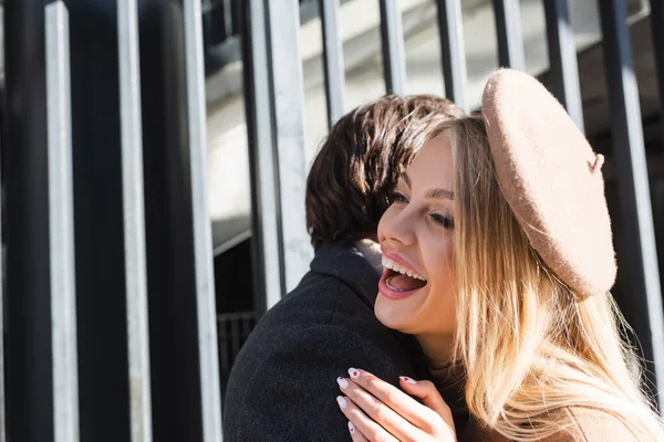 Aufgeregte blonde Frau mit Baskenmütze lacht neben Freund im Freien — Stockfoto
