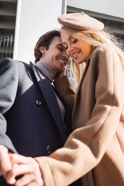 Vue à angle bas de la femme joyeuse touchant le visage du jeune homme et tenant sa main à l'extérieur — Photo de stock