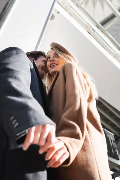 Vista de ángulo bajo de pareja romántica en ropa de otoño cogida de la mano al aire libre - foto de stock