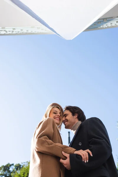 Низький кут зору щасливої пари в осінніх пальто на блакитне небо — стокове фото