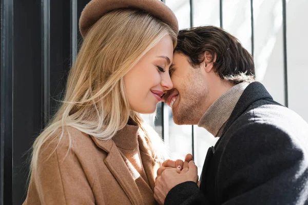 Vue latérale de la femme blonde en béret souriant près de l'homme tenant ses mains à l'extérieur — Photo de stock