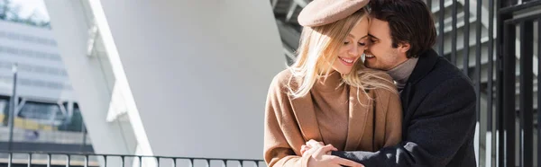 Uomo sorridente che abbraccia donna in berretto e cappotto autunnale all'aperto, banner — Foto stock