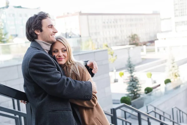 Young man in autumn coat hugging blonde girlfriend in city — Stock Photo