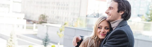 Hombre alegre mirando hacia otro lado mientras abraza novia en la ciudad, bandera - foto de stock