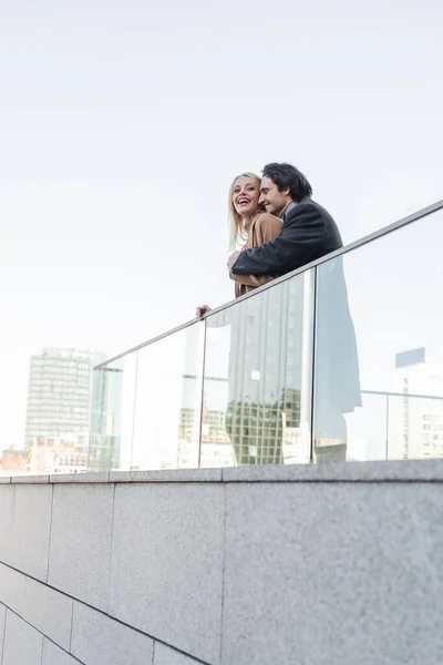 Hombre en abrigo abrazando riendo mujer cerca de valla de vidrio — Stock Photo