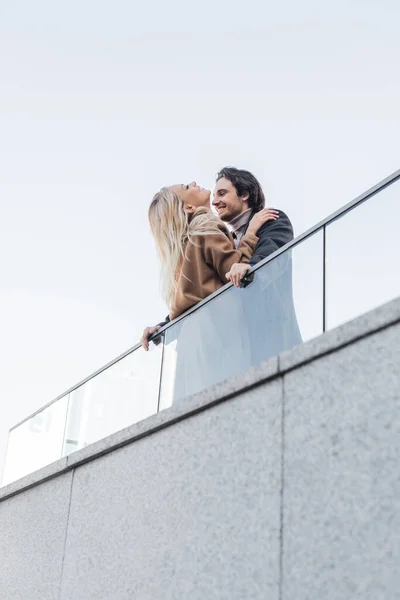 Low angle view of cheerful couple in love standing near glass fence — Stock Photo
