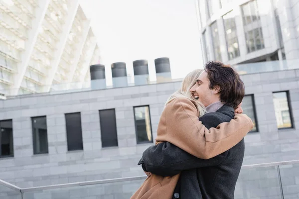 Side view of romantic couple in autumn coats embracing on urban street — Stock Photo