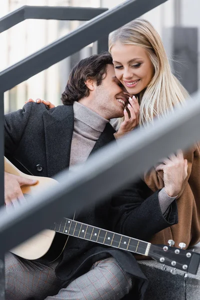 Junge blonde Frau lächelt neben Mann mit Akustikgitarre im verschwommenen Vordergrund — Stockfoto