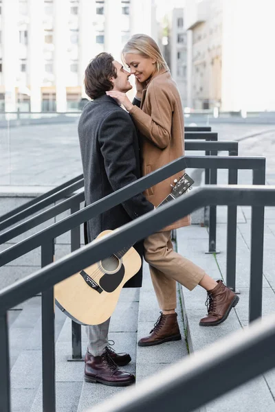 Vista lateral do homem com guitarra acústica em pé na escada cara a cara com mulher feliz — Fotografia de Stock