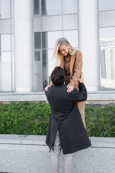 Uomo in cappotto autunno sostenere donna allegra in piedi su parapetto all'aperto — Foto stock