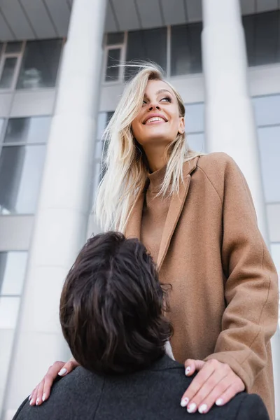 Mann erzieht fröhliche blonde Frau im Mantel auf Stadtstraße — Stockfoto