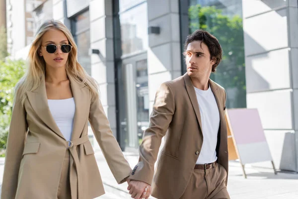 Young brunette man looking at stylish girlfriend in sunglasses while walking in city — Stock Photo