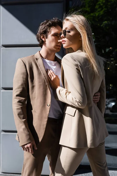 Blonde woman in sunglasses looking away near man embracing her on street — Stock Photo